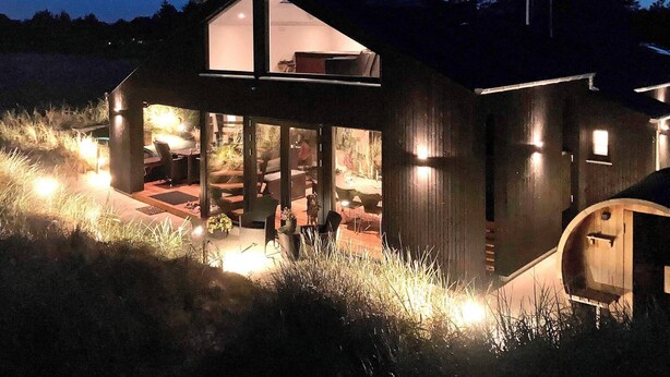 A modern house with a large glass extension, outdoor seating, and a well-lit patio area. - 5 Star Holiday Home in Albaek (Aalbaek)