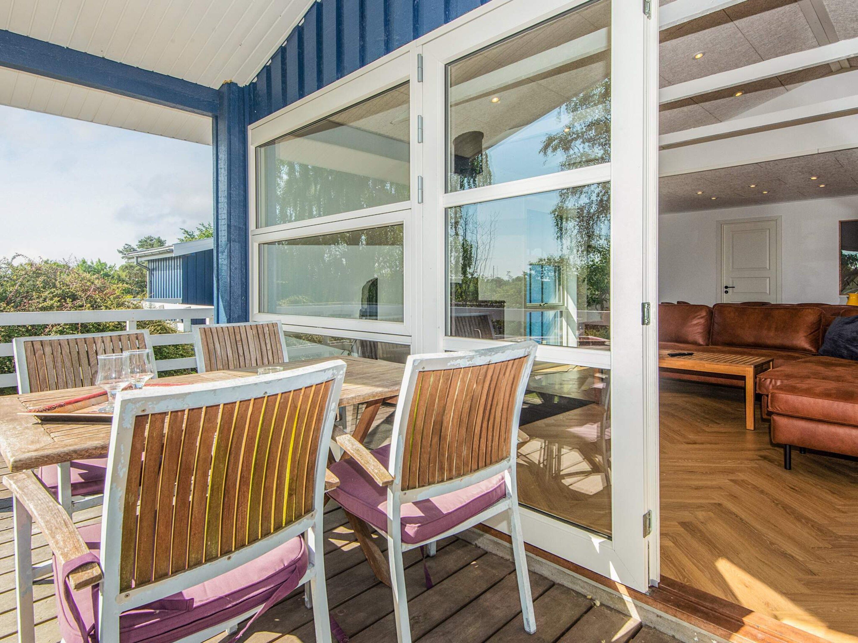 An outdoor patio with wooden furniture and large windows.