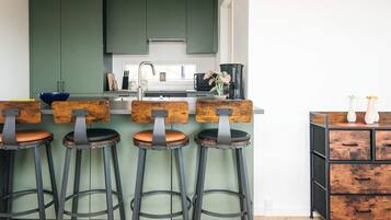 A kitchen with green cabinets, a stainless steel sink, and four bar stools with wooden seats and metal frames.
