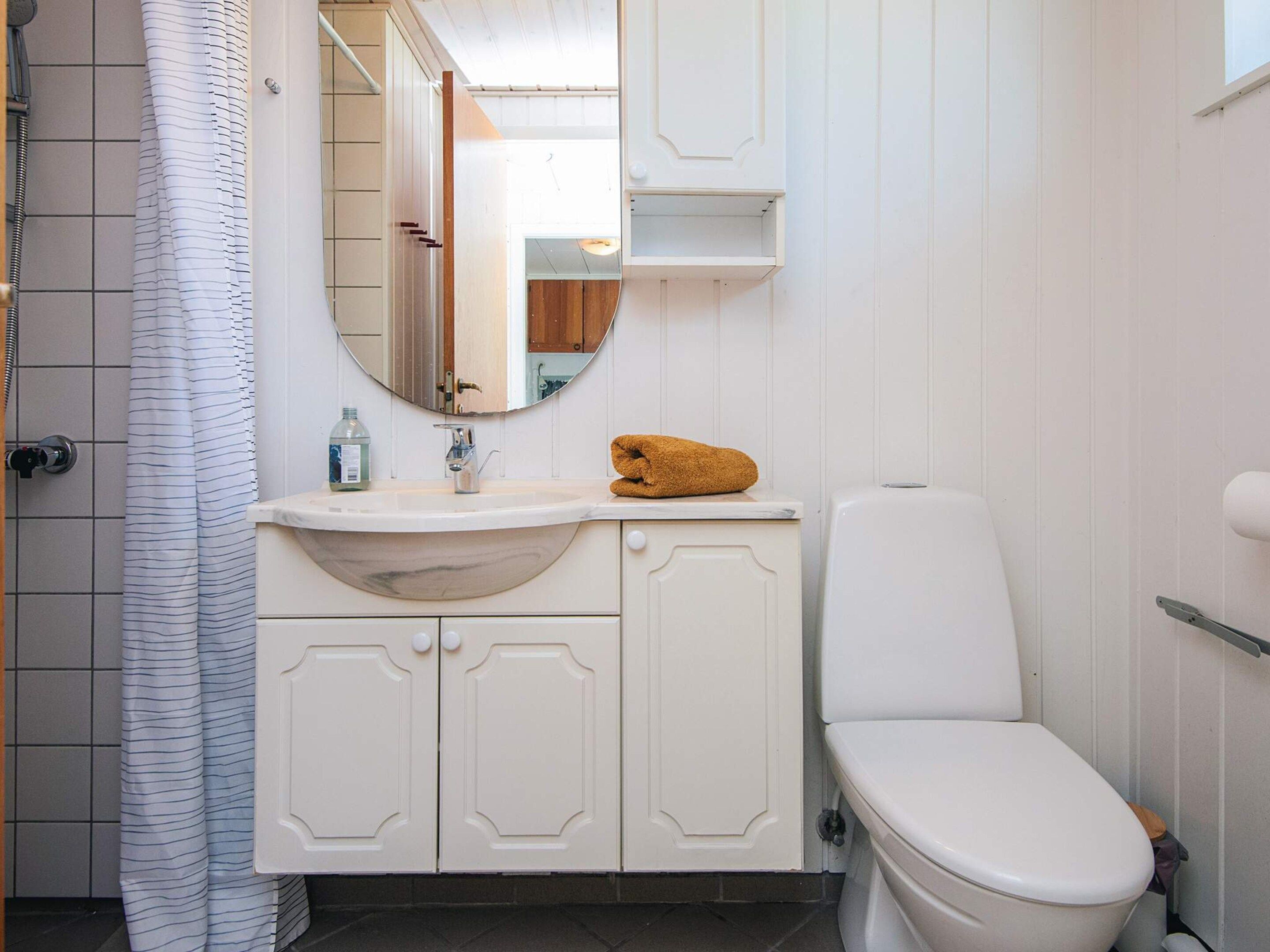 Ein Badezimmer mit weißem Waschbecken, einem Spiegel, einer Toilette und einer Duschvorhang.