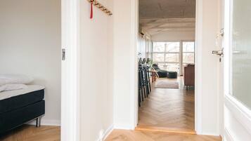 A room with a bed, a wooden floor, a door leading to another room with a sofa and chairs.