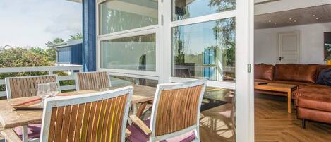 An outdoor patio area with wooden furniture and large windows.