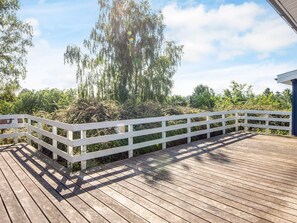 Una terraza de madera con barandillas blancas, rodeada de follaje y árboles.