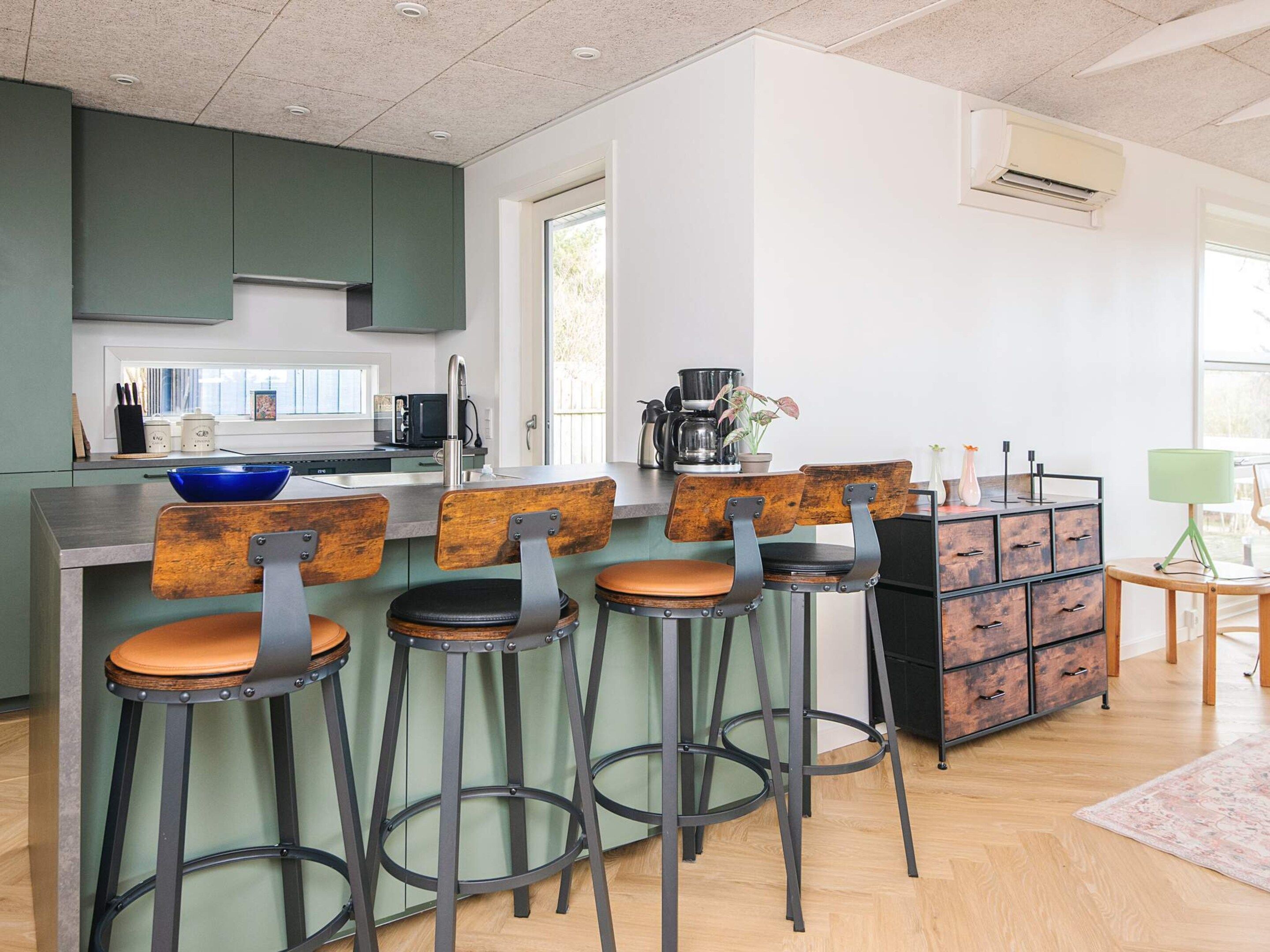 A modern kitchen with green cabinets, a bar area with stools, a coffee machine, and a view of the outdoors.