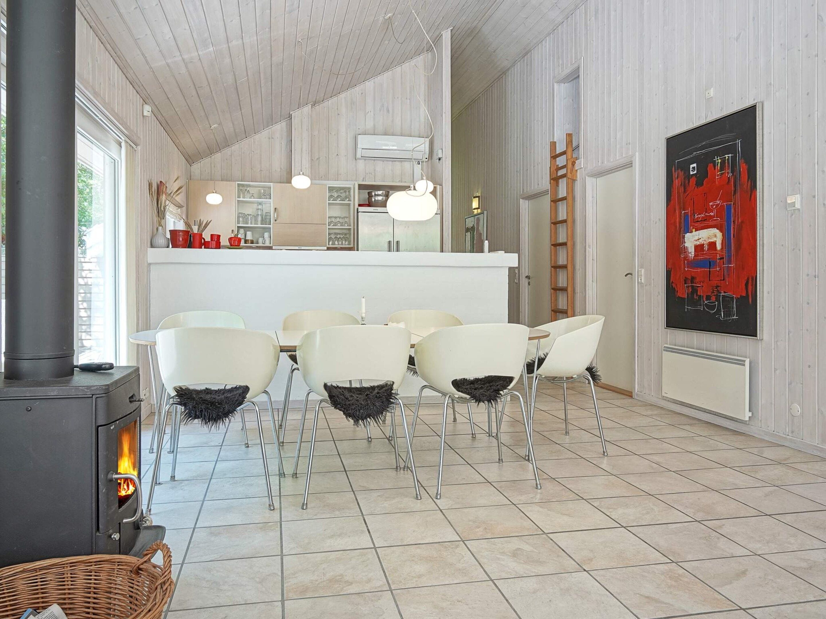 A modern kitchen with white cabinets, a central island, and a dining area with white chairs.