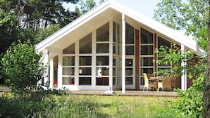 Un bâtiment moderne doté de grandes fenêtres et d’un toit en pente, entouré de verdure.