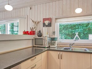 A kitchen with wooden cabinets, a microwave, a kettle, and a window with a view of greenery. - 5 Star Holiday Home in Aakirkeby (Akirkeby)