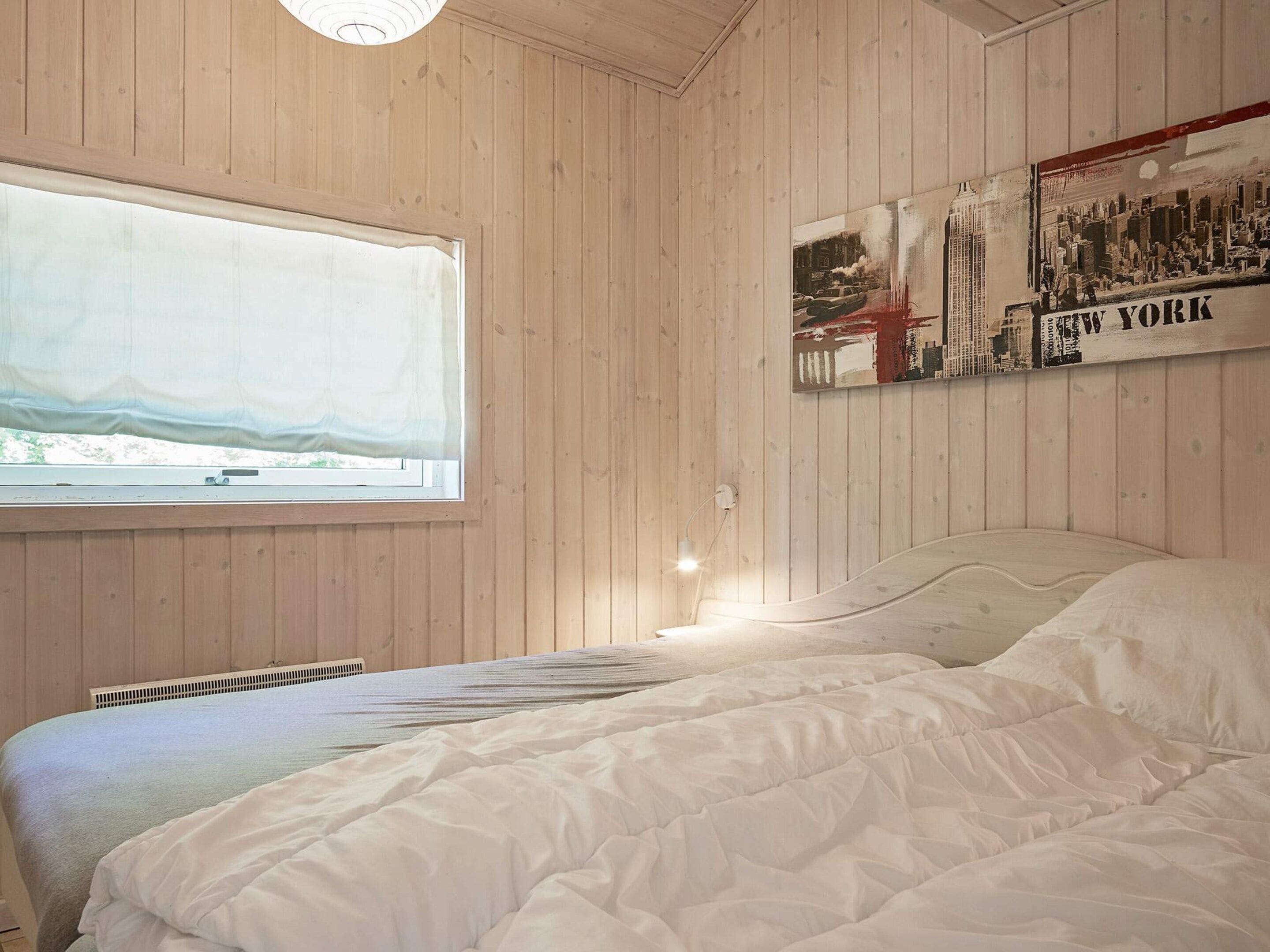 A room with wooden panel walls, a large window with a view, a bed with white bedding, and a poster of New York City.