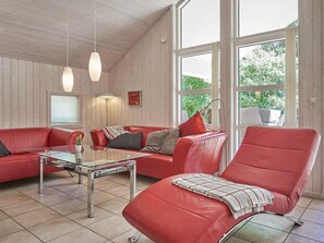 A modern living room with a red leather sofa, a glass coffee table, and a large window providing a view of greenery outside. - 5 Star Holiday Home in Aakirkeby (Akirkeby)