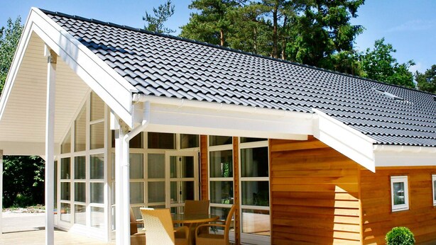 A modern wooden house with a covered patio, large windows, and a tiled roof. - 5 Star Holiday Home in Aakirkeby (Akirkeby)