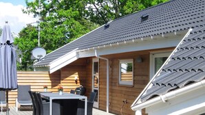 A wooden deck with a table and chairs, a satellite dish, and a small window. - 5 Star Holiday Home in Aakirkeby (Akirkeby)