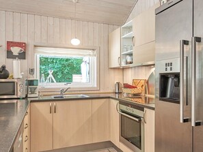 Une cuisine moderne avec des meubles en bois, un four encastré, une machine à café et une fenêtre donnant sur un paysage verdoyant.
