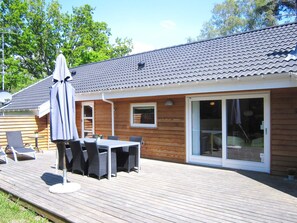 A wooden deck with a table and chairs, a covered umbrella, and a sliding glass door. - 5 Star Holiday Home in Aakirkeby (Akirkeby)