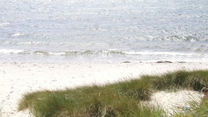 Une plage avec du sable et de l’herbe au premier plan, et une mer calme à l’arrière-plan.