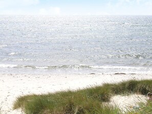 A beach with sand and grass in the foreground and a calm sea in the background. - 5 Star Holiday Home in Aakirkeby (Akirkeby)