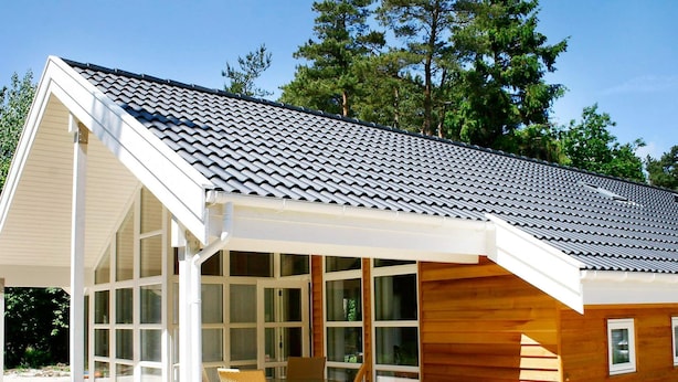Une maison moderne dotée d’un porche abrité, de grandes fenêtres et d’une façade en bois.