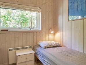A room with a bed, a bedside table, a window with a view of trees, and a wall-mounted light fixture. - 5 Star Holiday Home in Aakirkeby (Akirkeby)