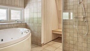 A modern bathroom with a freestanding bathtub, a glass-enclosed shower, and a wooden bench. - 5 Star Holiday Home in Aakirkeby (Akirkeby)