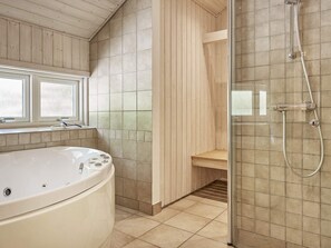 A modern bathroom with a freestanding bathtub, a glass-enclosed shower, and a wooden bench. - 5 Star Holiday Home in Aakirkeby (Akirkeby)