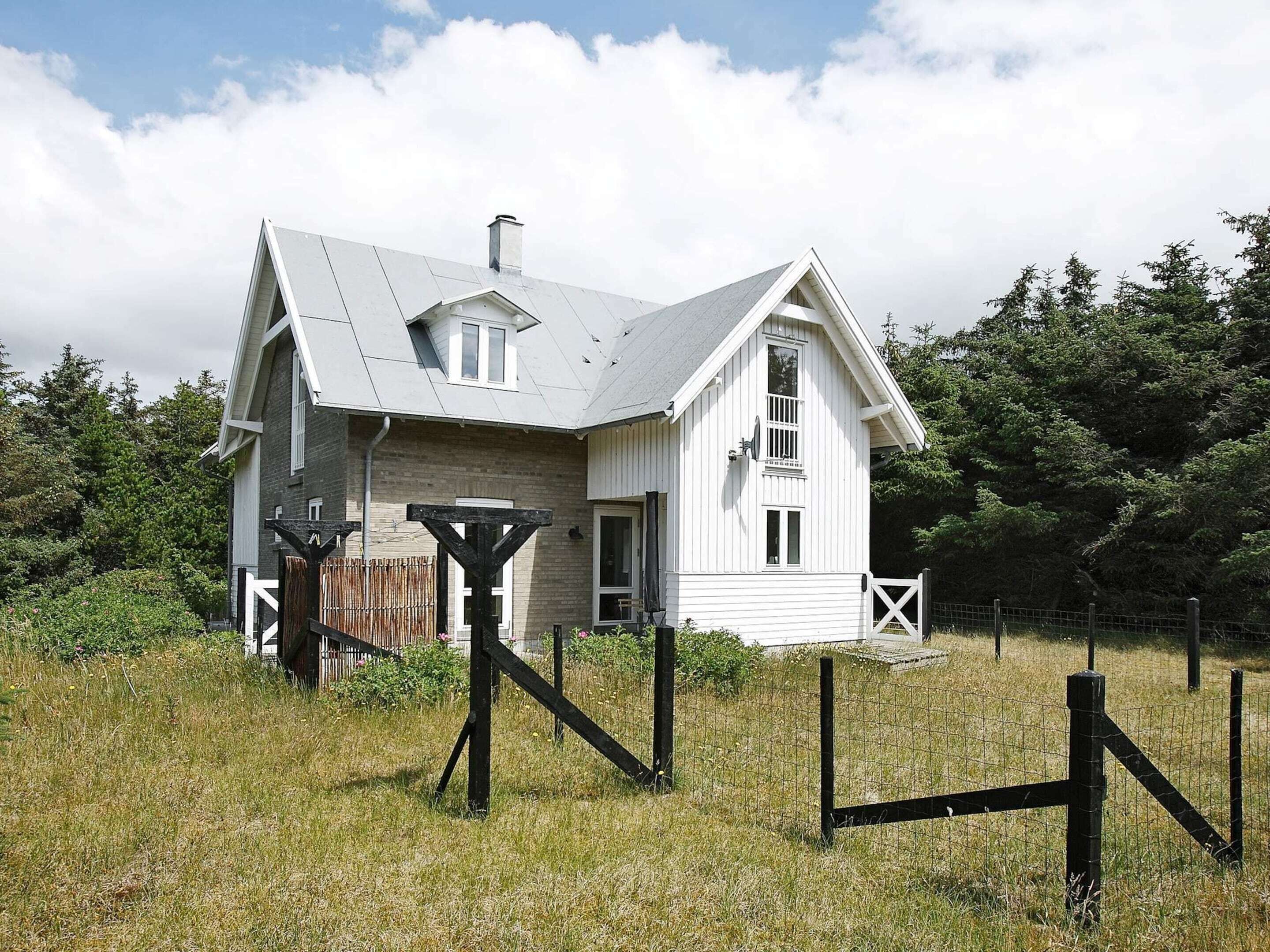 A white house with a gabled roof, surrounded by a wooden fence and a grassy field.