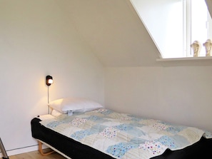 A small, single-bed room with a slanted ceiling, a bedside lamp, a white pillow, and a floral-patterned bedspread. - Delicate Holiday Home in Harboøre near Sea (Harboore)