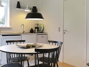 Une cuisine compacte avec une table de salle à manger ronde, des chaises noires, un luminaire suspendu noir et un lave-vaisselle Siemens.