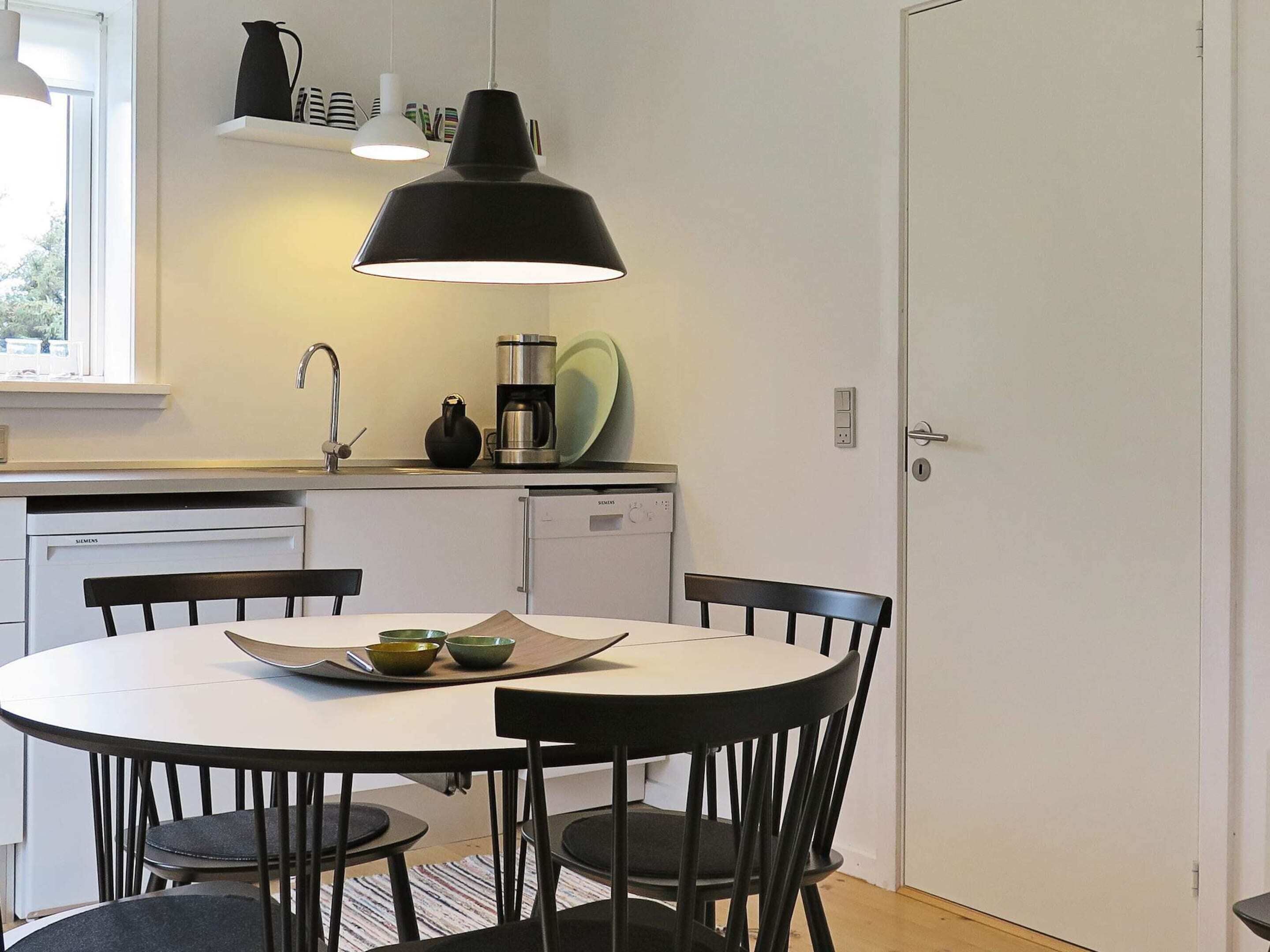 A compact kitchen with a white table, black chairs, a black pendant light, and a Siemens dishwasher.