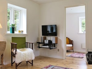 Un salon avec un téléviseur, une petite table, une chaise et une fenêtre agrémentée d’une plante.