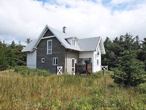 Une maison à deux étages, avec un toit à pignon, une cheminée et une cour clôturée.
