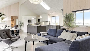 A modern living room with a sofa, coffee table, and dining area. - 5 Star Holiday Home in Vaeggerlose (Vaeggerlose)