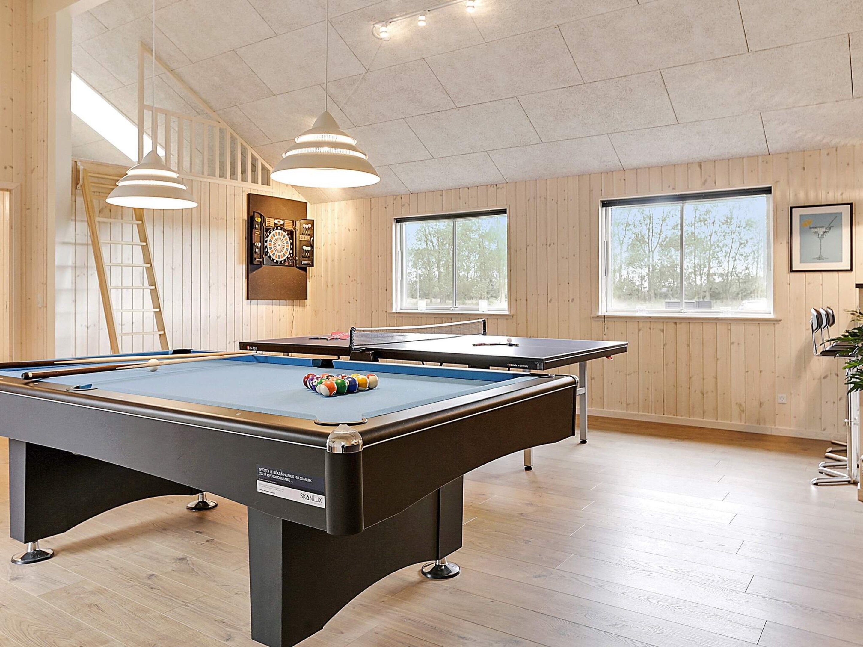 Un tavolo da biliardo con un bersaglio di freccette e palle da biliardo, pavimenti in legno e ampie finestre.