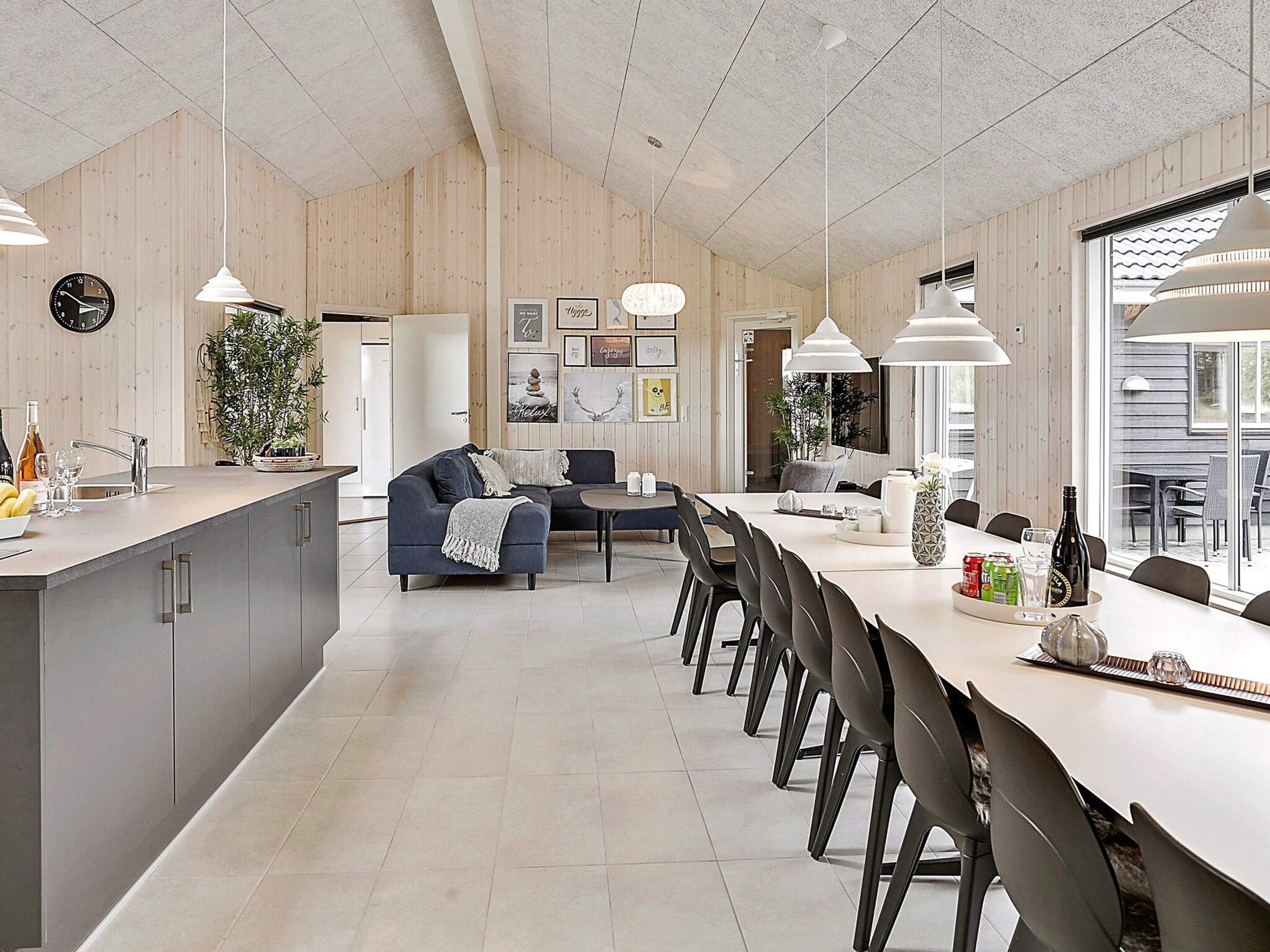 Una cocina moderna con comedor, paredes de madera, iluminación colgante y vistas a través de un ventanal.