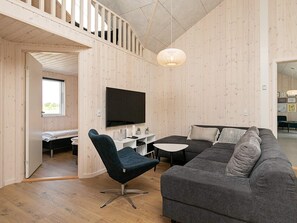 A modern living room with a flat-screen TV, a dark sofa, a round table, and a unique hanging light fixture.