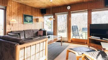 A cabin interior with a wooden ceiling, a sofa, a television, and a dining area.