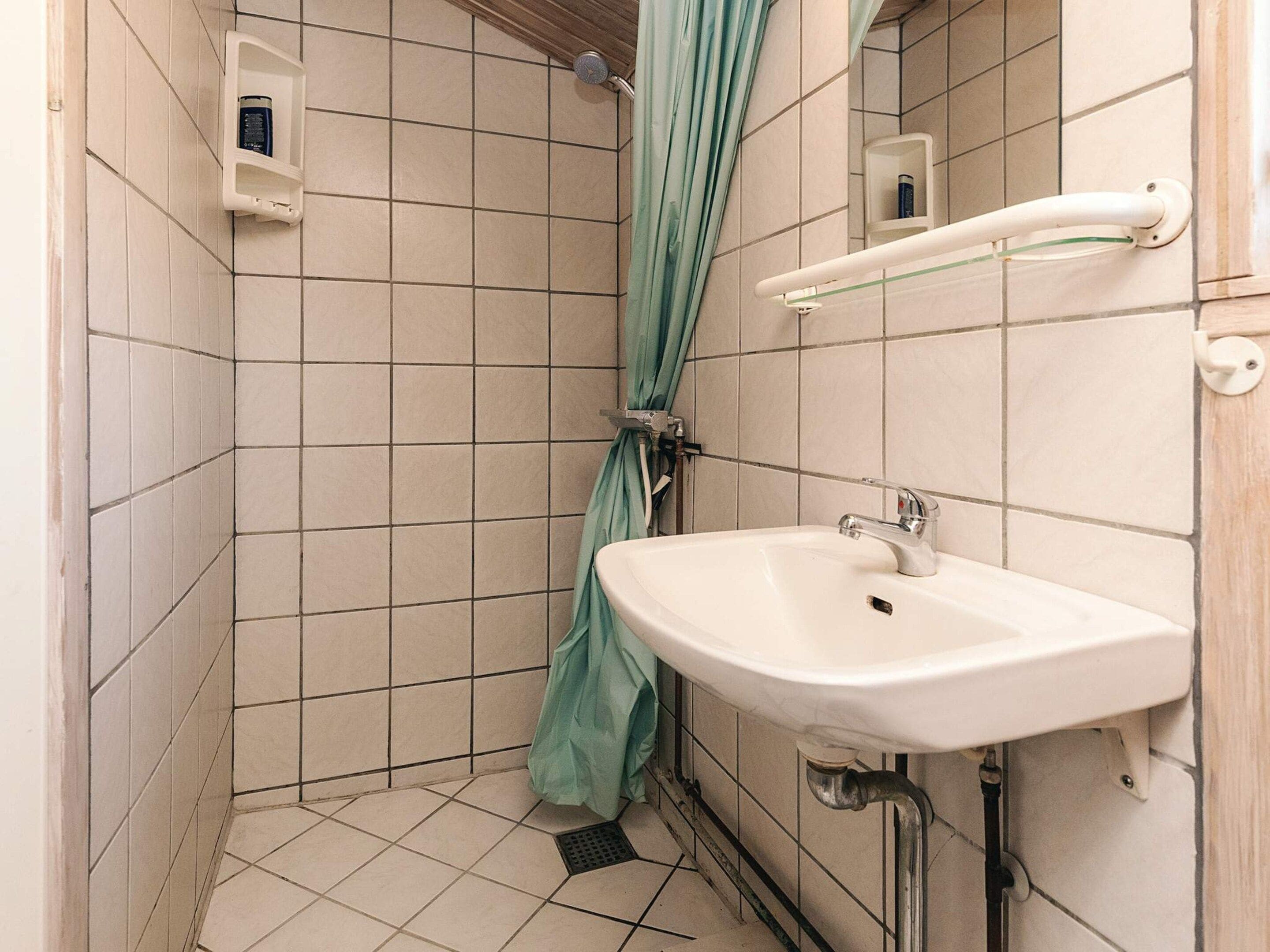 A bathroom with a white sink, a shower curtain, and a small shelf with toiletries.