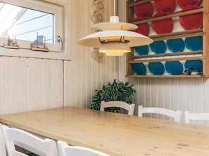 A wooden dining table with white chairs, a hanging pendant light, and a wall-mounted shelf with colorful plates. - Spacious Holiday Home in KarrebÃ¦ksminde near Fishing (Karrebæksminde)