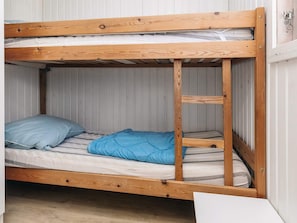 Un lit superposé à deux niveaux, avec une structure en bois et un matelas recouvert d’une couverture bleue.