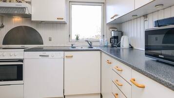 A modern kitchen with white cabinetry, a built-in oven, a dishwasher, a coffee maker, and a microwave.
