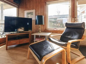 A room with a television, a lamp, a chair, and a table.