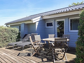 Une terrasse avec des meubles d’extérieur, une maison à la façade bleue et un ciel dégagé.