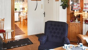 A dining area with a table set for four, a blue armchair, a wooden cabinet, and a kitchen area visible through an open door. - 6 Person Holiday Home in Sæbø (Orsta)