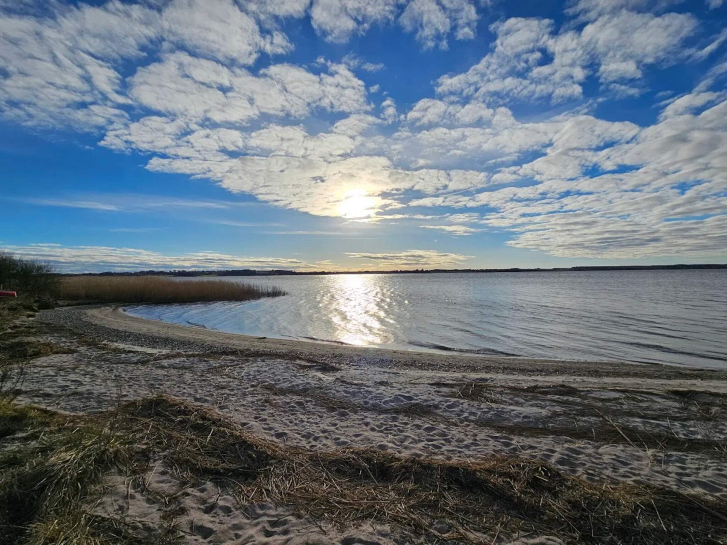 Uma praia com céu claro e o sol refletindo na água.
