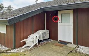 Un edifici amb una porta vermella, un aparell d'aire condicionat i una cadira blanca a l'exterior.