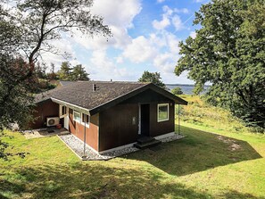 A small wooden cabin with a sloped roof, a porch, and a view of a lake.