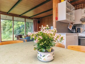 A dining table with a potted plant in the center, a wooden ceiling, and a kitchen area in the background. - 8 Person Holiday Home in Skals (Skals)