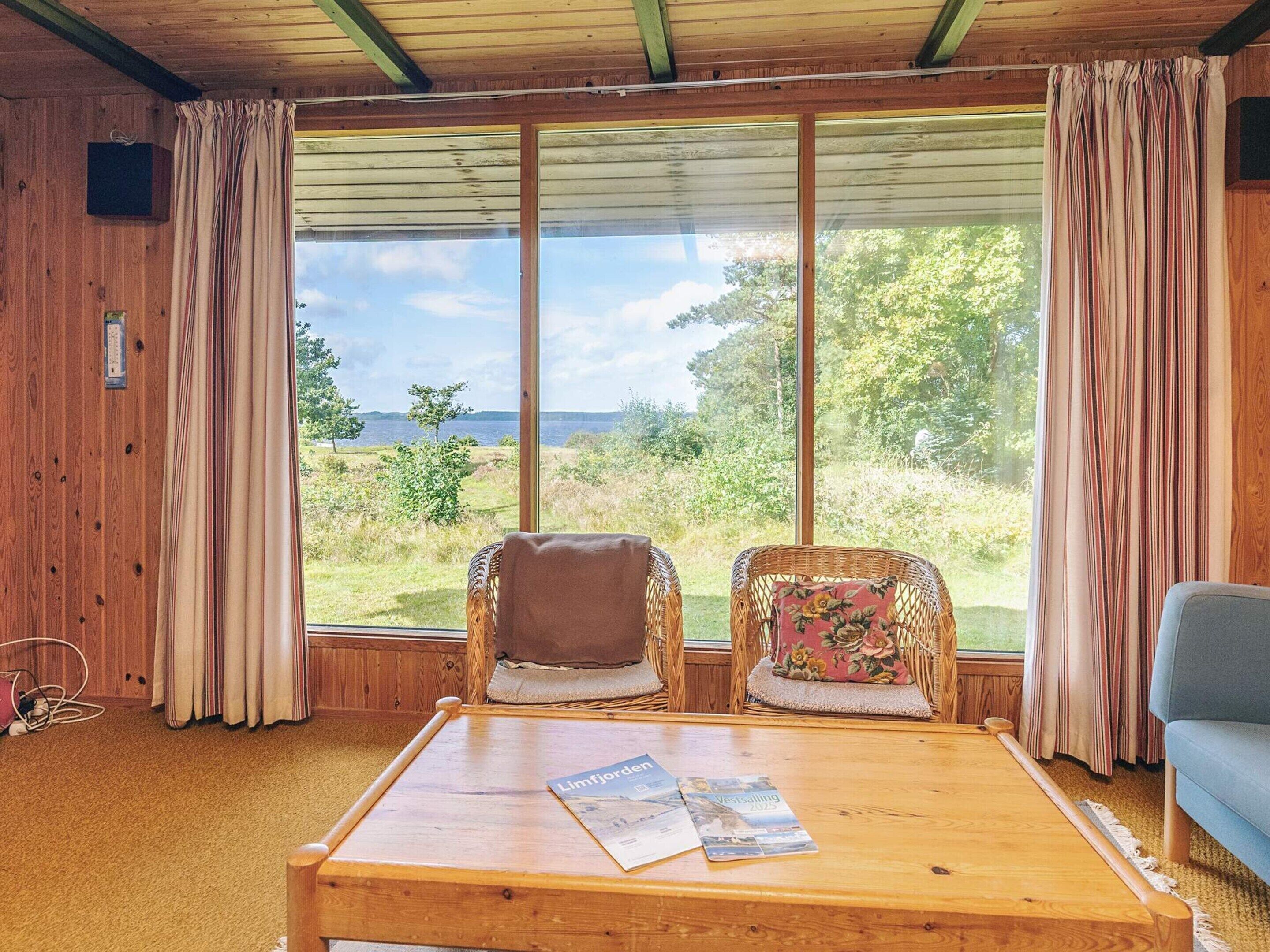 A room with two wicker chairs, a wooden table with magazines, and a view of the outdoors.