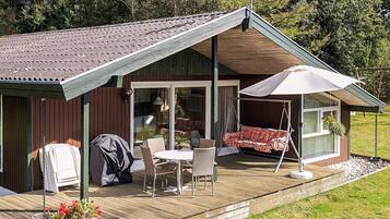 Una terraza de madera con porche cubierto, mobiliario exterior y una parrilla.