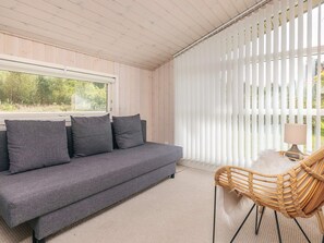 Ein modernes Interieur mit einem grauen Sofa, einem Korbstuhl und einem Fenster mit weißen Jalousien.