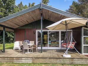 Una terraza techada con mobiliario exterior, una silla colgante y un paraguas grande.