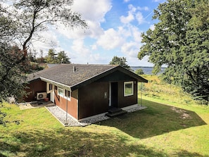 A small wooden cabin with a sloped roof, a front porch, and a view of a lake.